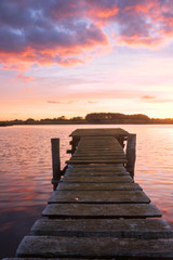 Fototapeta na wymiar rustikaler Steg mit Moos am See mit angestrahlten Wolken am Abendhimmel, Hochformat