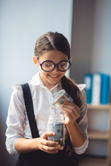 Girl in white shirt putting money into a jar and smiling