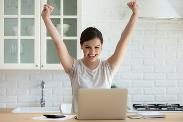 I did it. Happy millennial woman employee working online by laptop from home is excited of...