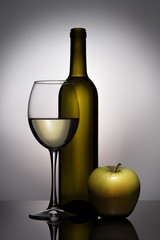 Stylish, modern still life with glass objects (a wine bottle and a wine glass) and an apple.