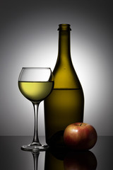 Stylish, modern still life with glass objects (a wine bottle and a wine glass) and an red apple.