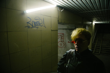 A suspicious person stands in the light of neon lamps in an underground passage.