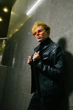A man in a black leather jacket stands against the wall. Fashion and Style.