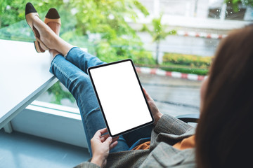 Mockup image of a woman holding and using digital tablet with blank white desktop screen while sitting in office
