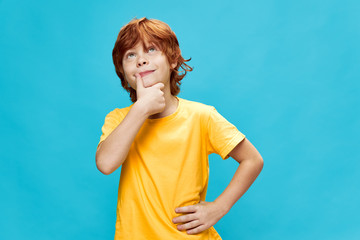 interested red haired child in a yellow T-shirt holds his hands at the waist