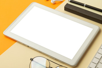 Tablet computer screen mockup with clipping path and wireless earphones, notebook, keyboard, glasses, pen on vibrant orange background.
