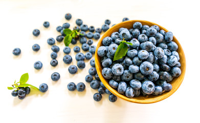 A scattering of blueberries on the table and in a wooden bowl