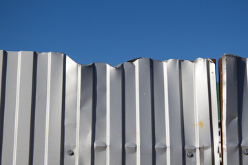 Metal bent dirty gray fence and blue sky