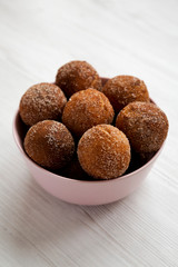 Homemade Fried Donut Holes in a pink bowl on a white wooden background, side view.