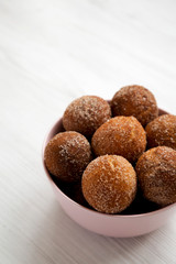 Homemade Fried Donut Holes in a pink bowl on a white wooden table, side view. Copy space.