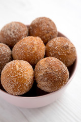 Homemade Fried Donut Holes in a pink bowl on a white wooden background, side view. Close-up.
