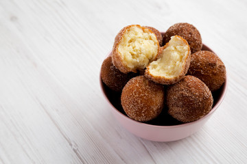 Homemade Fried Donut Holes in a pink bowl on a white wooden background, side view. Copy space.