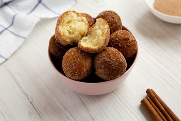 Homemade Fried Donut Holes in a pink bowl on a white wooden background, side view.