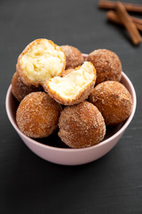 Homemade Fried Donut Holes in a pink bowl on a black background, side view.