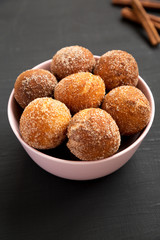 Homemade Fried Donut Holes in a pink bowl on a black surface, low angle view.