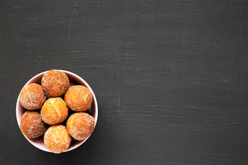 Homemade Fried Donut Holes in a pink bowl on a black background, top view. Flat lay, overhead, from...