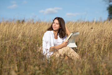Young European student woman with a book in a field in autumn or summer