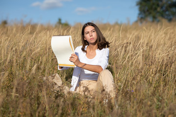 Young European student woman with a book in a field in autumn or summer