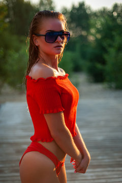 beautiful brunette model in a red sweater and dark glasses poses in front of the camera. Close-up and full-length shooting.
