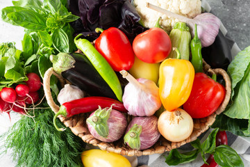 Assortment of vegetables in a basket on the table. A lot of different raw vegetables in the basket. Eggplant, tomatoes, garlic, sweet pepper, onion on the table. Healthy food concept