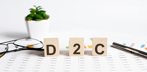 D2C word concept written on wooden blocks, cubes on a light table with flower ,pen and glasses on...