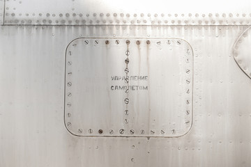 Old silver metal surface of the aircraft fuselage with rivets. Selected focus. Russian text - PLANE CONTROL 