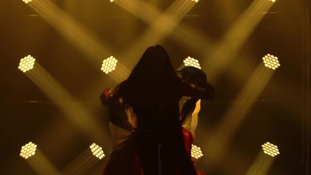 Girl dancing in a dark studio with smoke and yellow neon lights. Silhouette attractive brunette in a sexy suit in the color of the English flag and rhinestones. Contemporary female dance show.