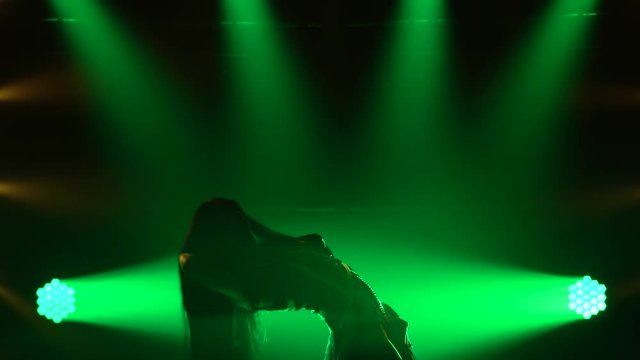 Sexy girl passionately dancing in dark studio with smoke and green neon lights. Silhouette attractive brunette in a sexy suit in the color of the English flag and rhinestones. Sexy female dance show.