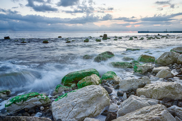 Fototapeta na wymiar Long exposure of the coastal landscape of Imereti Adler beach with warm evening light, when the waves wash over rocks covered with seaweed