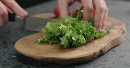 man chopping frisee salad leaves on olive board