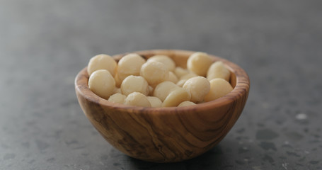 shelled macadamia nuts in olive wood bowl on terrazzo surface