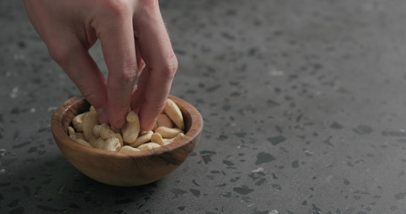 man hand takes cashew nuts from olive bowl on terrazzo countertop