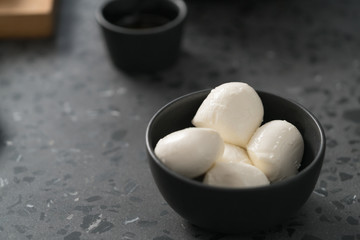 Small mozzarella balls in black bowl on concrete background