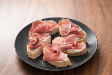 bruschetta with prosciutto and cream cheese on black plate on walnut background
