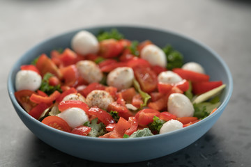 salad with mozzarella, tomatoes and bell pepper in blue bowl on kitchen countertop