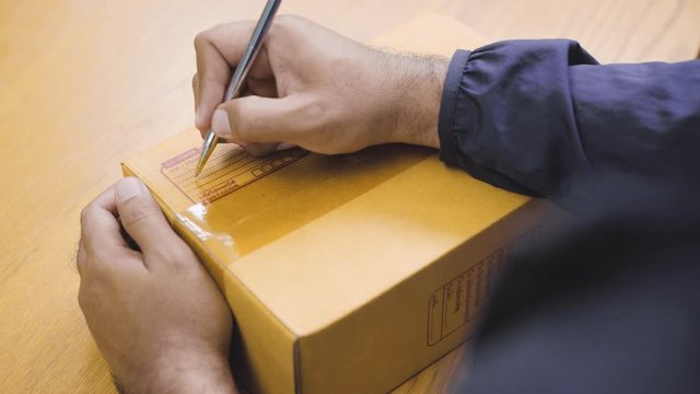 Close Up. Fast post shipment service concept. young asian man customer writing sender address on parcel cardboard box at home office desk. 4K Resolution.