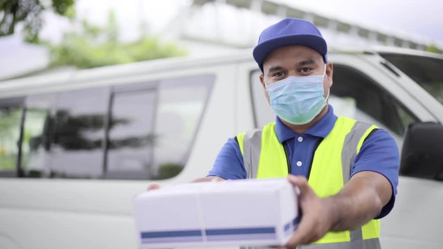 Fast post shipment service concept. Young asian deliveryman wear face mask to protect virus holding a cardboard at street and giving parcel. 4k Resolution.