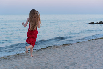 Fototapeta na wymiar A girl in a red dress runs along the seashore