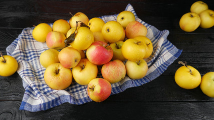 Lots of ripe yellow apples with dew drops on a white towel on a black wooden table.