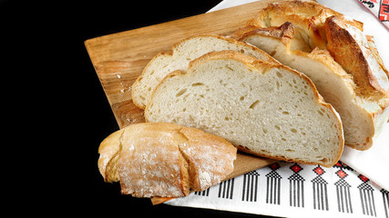 Homemade round white bread loaf cut into large slices on a cutting board on a black wooden table.