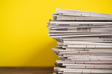close up newspapers folded and stacked on yellow background on the table