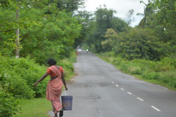 Poor woman walking in the Indian Village Road carrying water