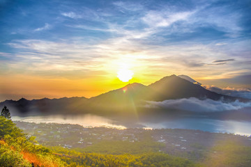 A scenic landscape view of cloud movement during the morning sunrise with golden sunbeam behind the mountain in Bali