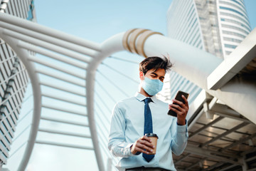 Young Asian Businessman Wearing a Surgical Mask and Using a Smart Phone in City. Healthcare in New Normal Lifestyle Concept