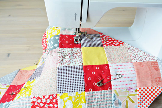 Working process: quilt, metal pins and sewing machine on wooden table
