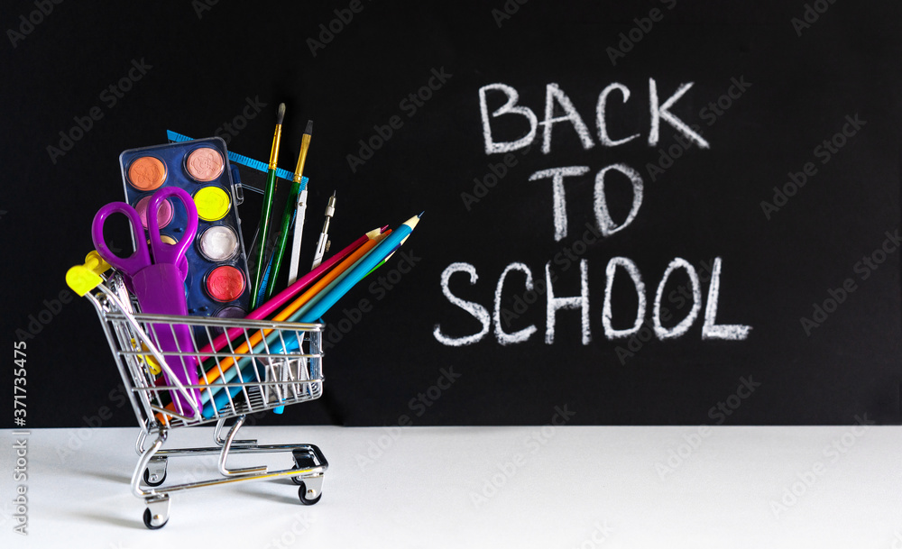 Wall mural back to school. mini shopping cart with pencils and school supplies on a black background with an in