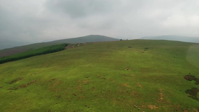 Aerial shot panning alone the side of a green hill in the English Lake District, cloudy day.