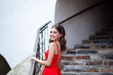 Portrait of a girl in the castle in a red dress. The girl is holding on to the stairs. Portrait of a girl.