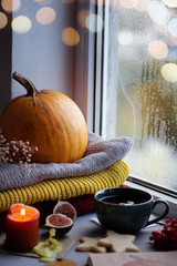 Autumn still life photography by the window, pumpkin, a cup of tea, candle, biscuits, sweaters, figs, bokeh.