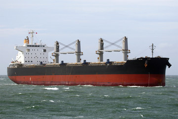 schwarzer Massengutfrachter mit Ladekränen erreicht den Hafen